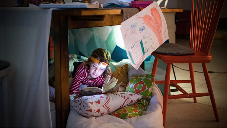 A young girl reading a book on her bed in a cozy room, illustrating the importance of quiet spaces for creativity and relaxation.